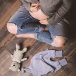 Schwangere sitzend mit Teddy und Strampler